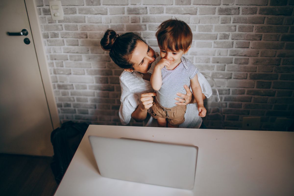 Mãe trabalhando com notebook enquanto cuida do filho pequeno, ilustrando redução de jornada para pais de criança com autismo